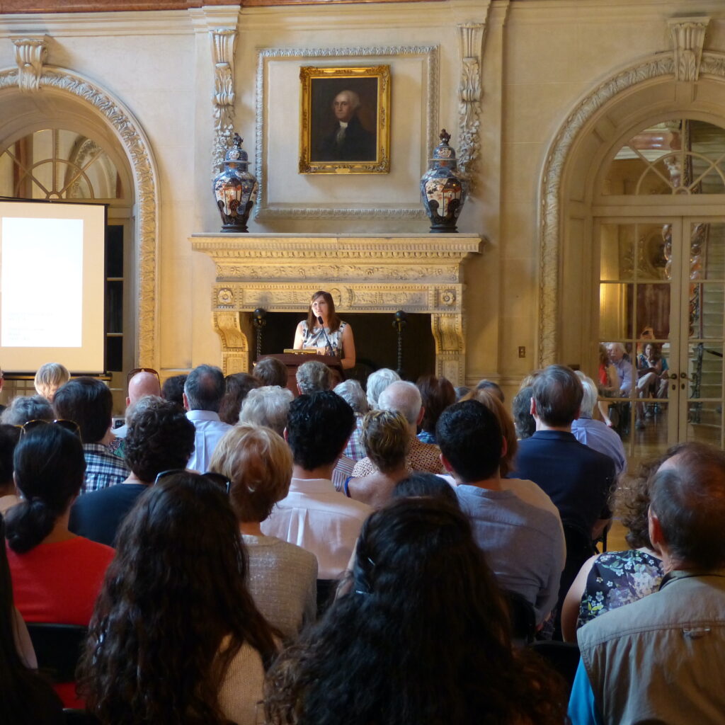 Image of Curator Emily Parsons speaking to an audience at a public program in the Ballroom of Anderson House.